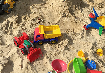 Sandkiste mit Plastikbagger, Plastiktrecker und weiteren Plastik- Spielsachen